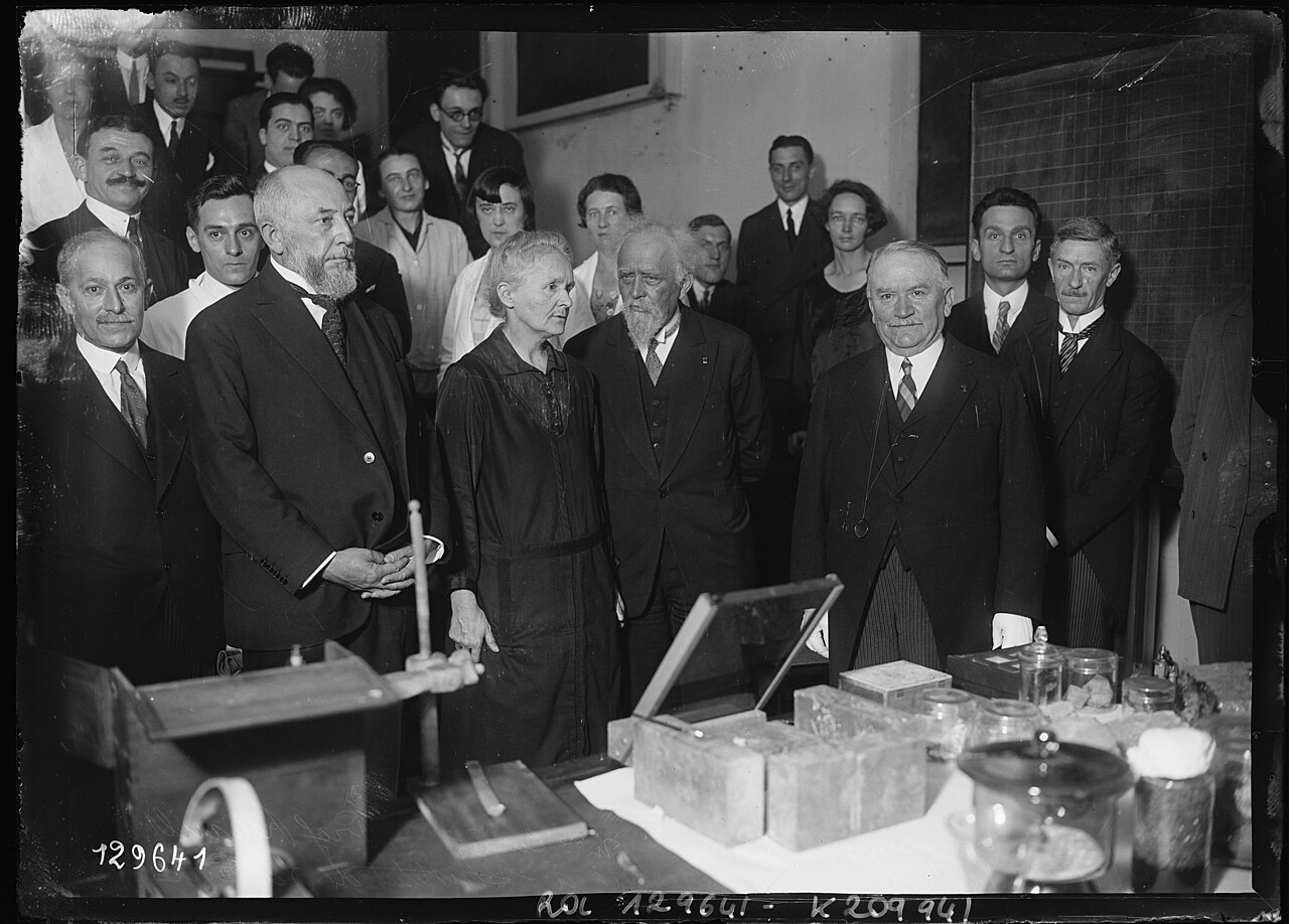 Marie Curie, Jean Perrin et le président Doumergue entourés de chercheurs dans un laboratoire de l’Institut du radium